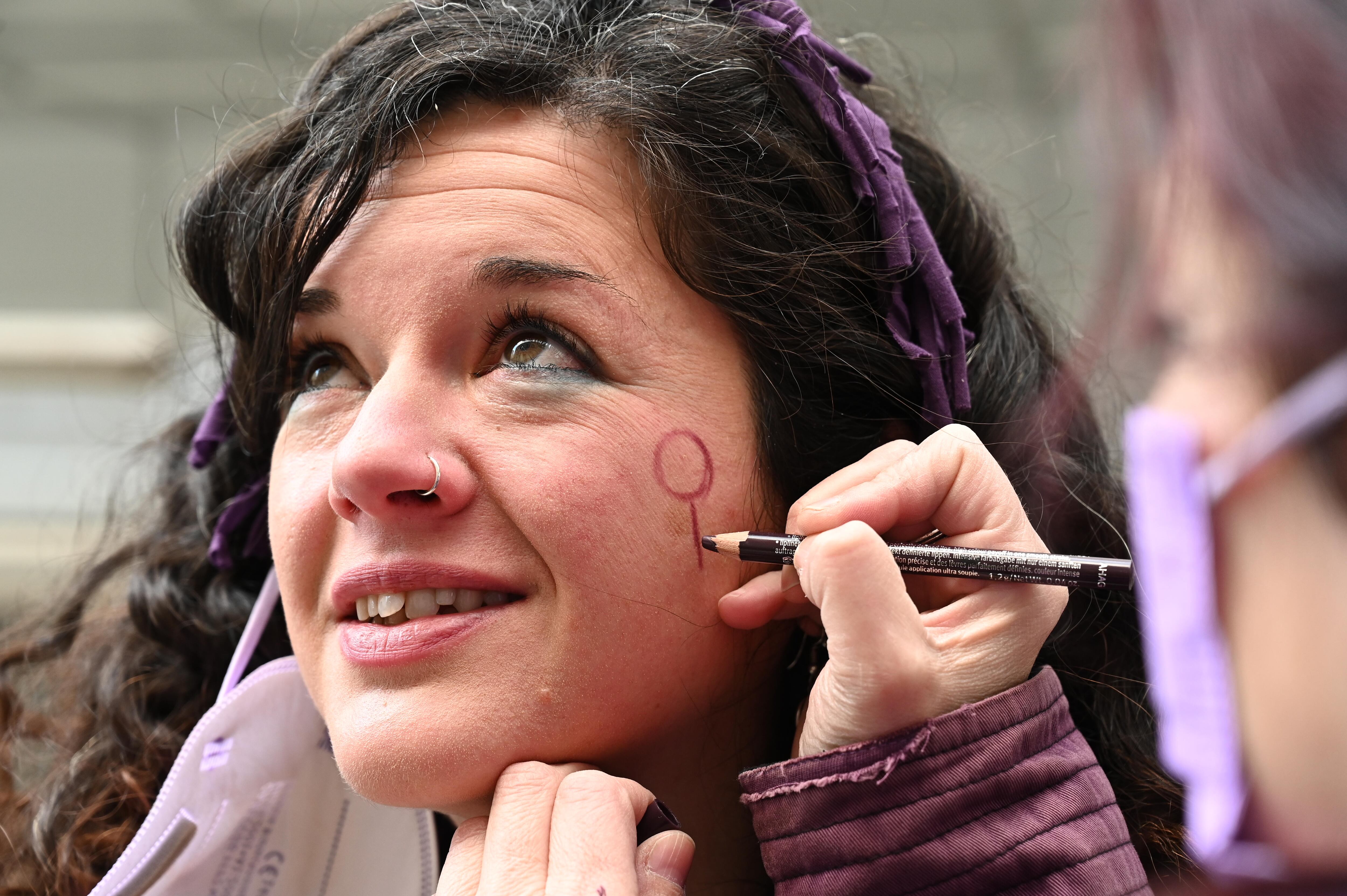 Una mujer pintándose el símbolo de la igualdad en la cara por el 8M.