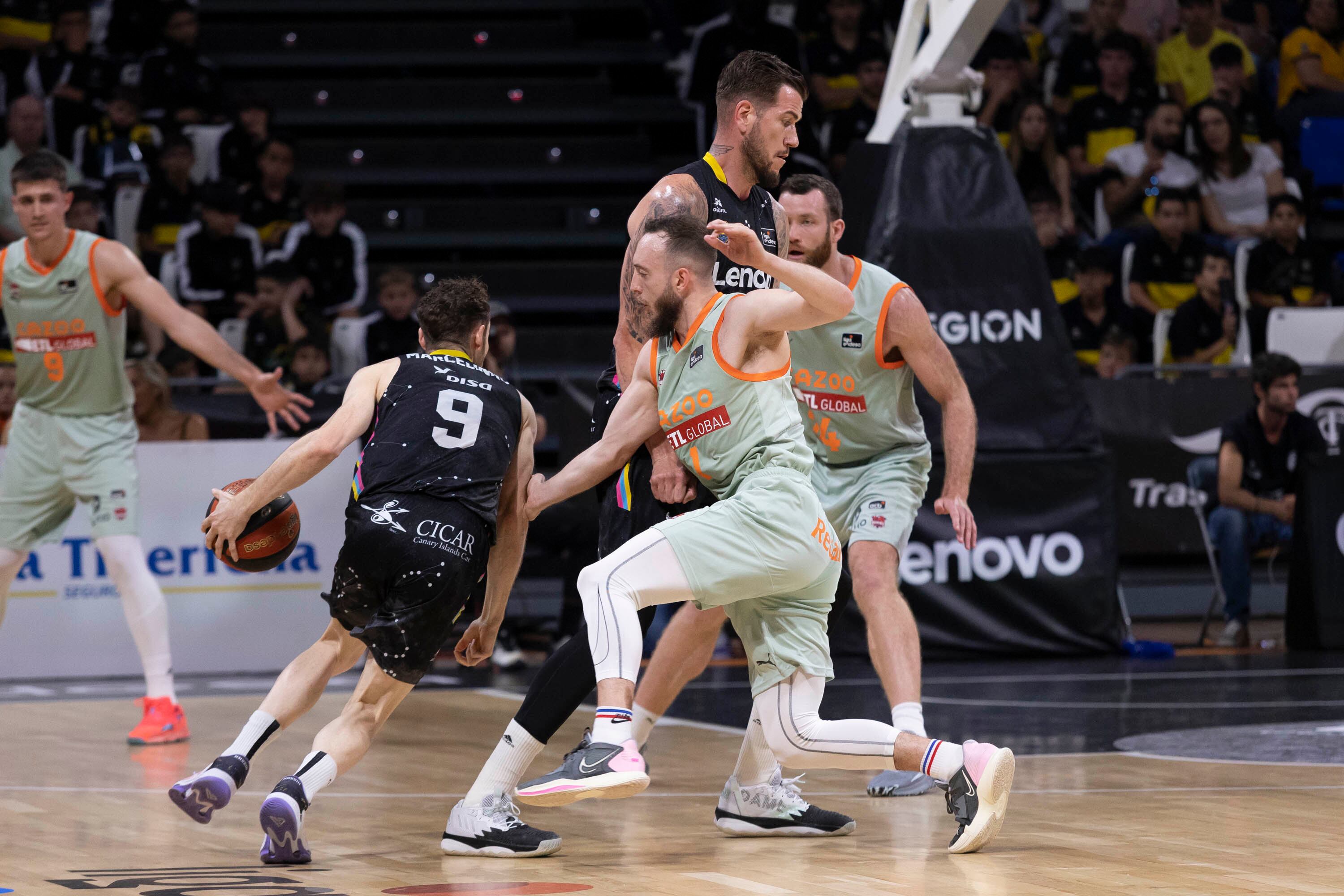 Fran Guerra (c) bloquea al base del Baskonia Max Heidegger (d), ante el avance del base del Lenovo Tenerife, Marcelinho Huertas (i).