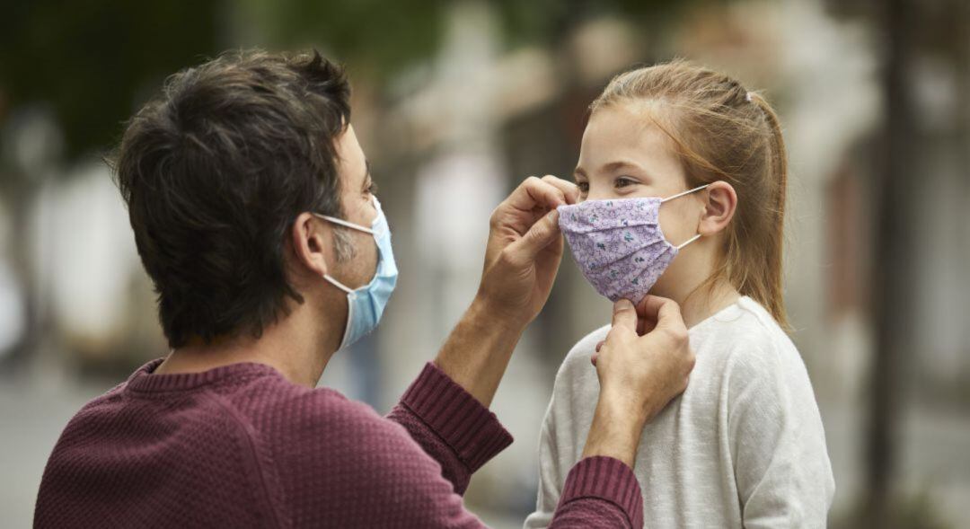 Un adulto coloca una mascarilla a una niña