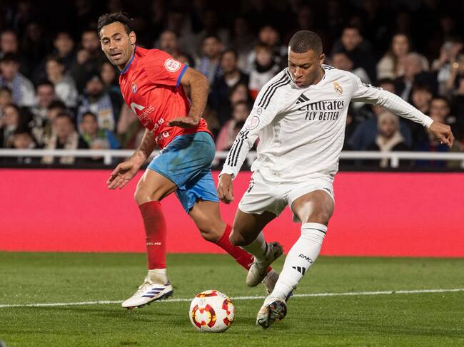 El delantero francés del Real Madrid Kylian Mbappé (d) dispara a puerta ante el jugador de la Deportiva Minera Omar Perdomo (i).
