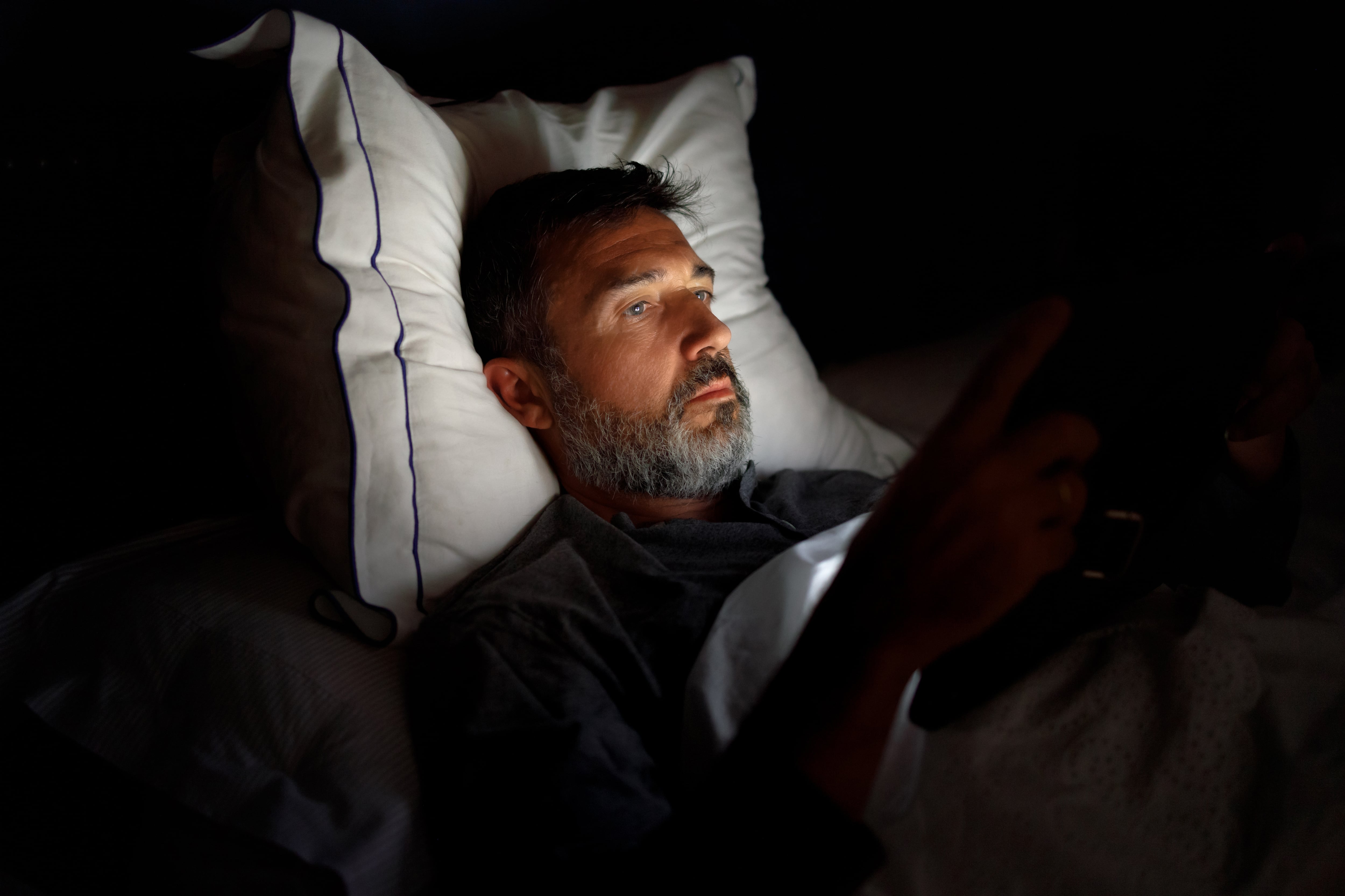 Atractive mature man with beard lying on bed using digital tablet.