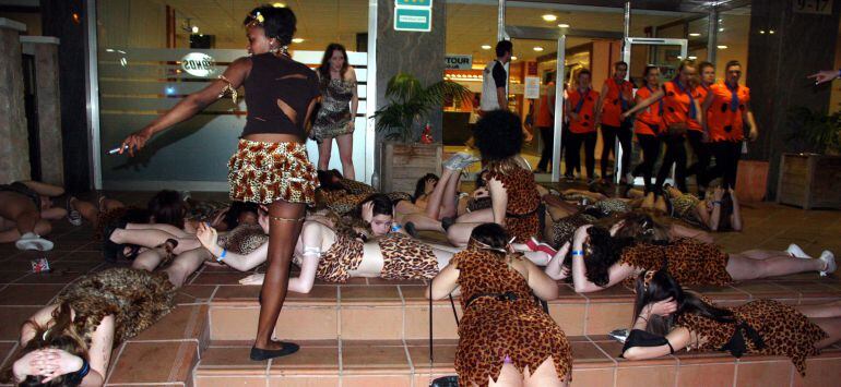 Un grup nombrós de noies disfressades, esteses al terra, com fent un mosaic, a les escales d'un hotel.