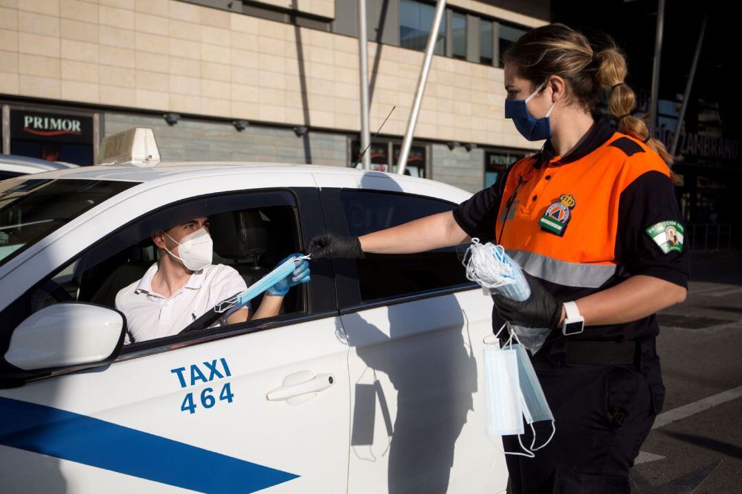 Una voluntaria de Protección Civil reparte una mascarilla a un taxista junto a la estación de tren María Zambrano de Málaga, hoy martes cuando el número total de casos por coronavirus en Andalucía se eleva a 14.394, 45 más que ayer lunes, lo que supone un incremento del 0,31 %, y el de muertos a 1.267, cuatro más que ayer, un 0,31 % más, según datos de la Consejería de Salud