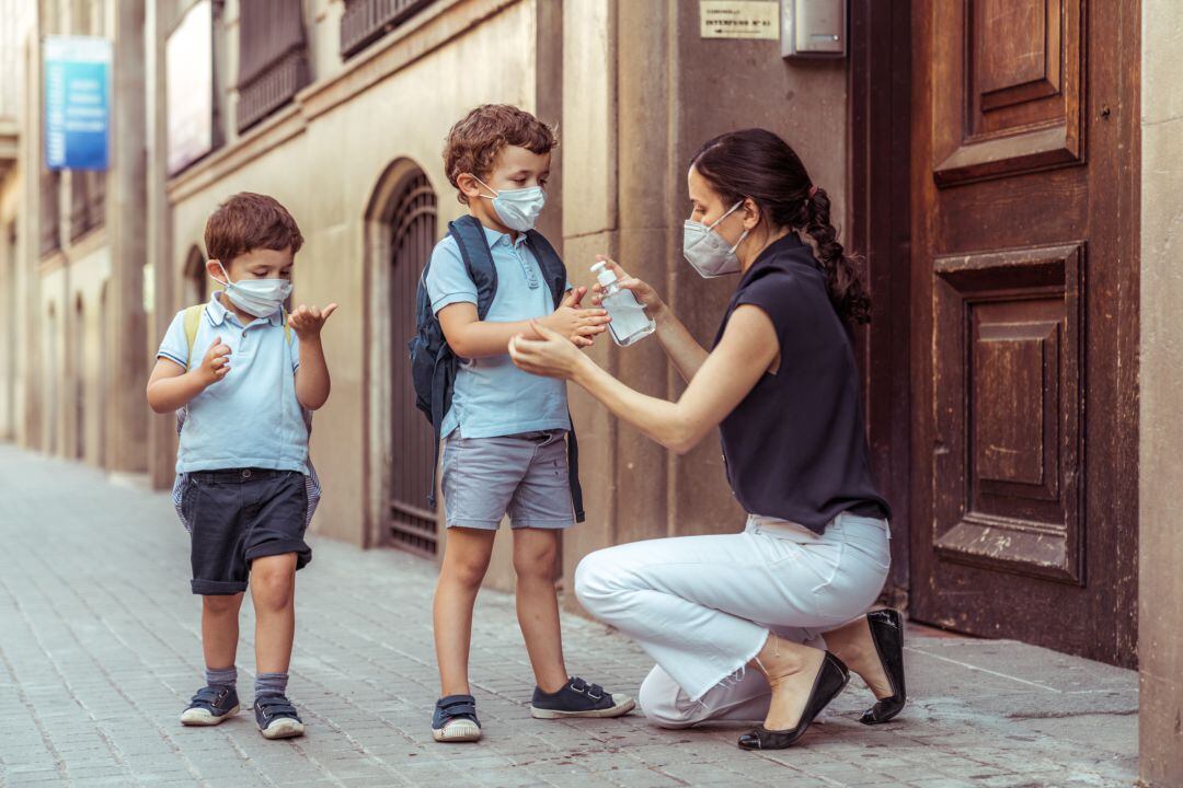 Una madre limpia las manos de sus hijos con gel hidroalcohólico al volver de clase