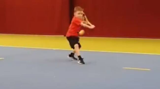 El pequeño Ethan se prepara para golpear la pelota de revés.