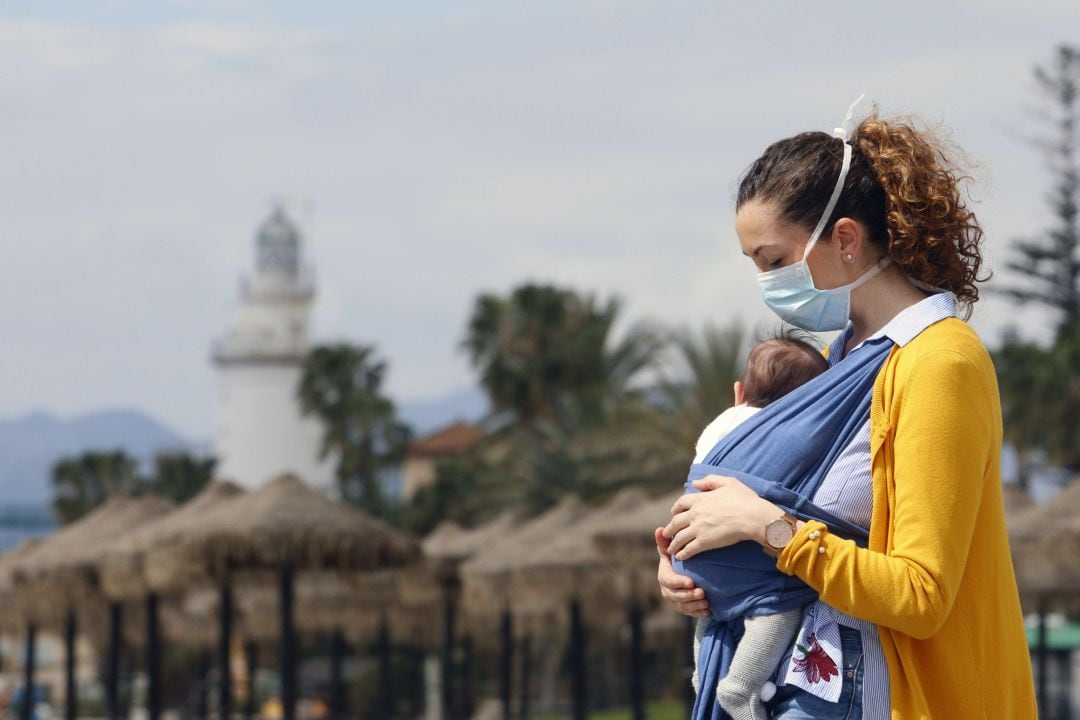 Una mujer protegida con una mascarilla da un paseo con su bebé.