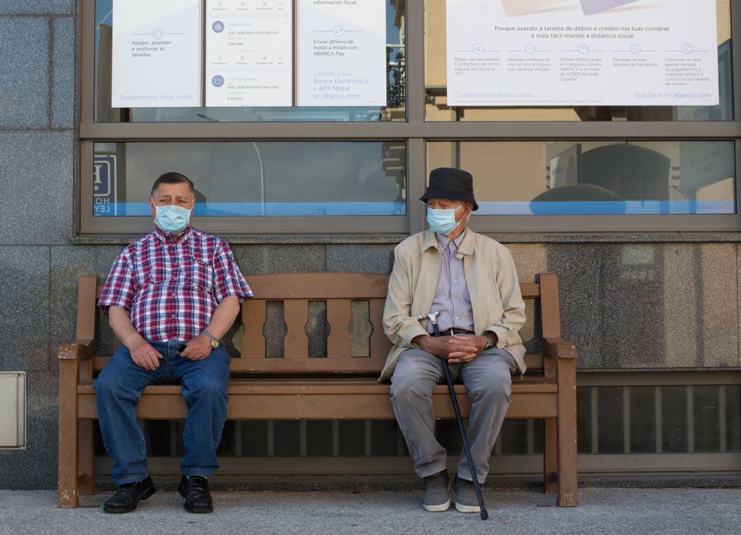 Dos hombres protegidos con mascarillas descansan en un banco en Foz, en la comarca de A Mariña, Lugo, Galicia (España)