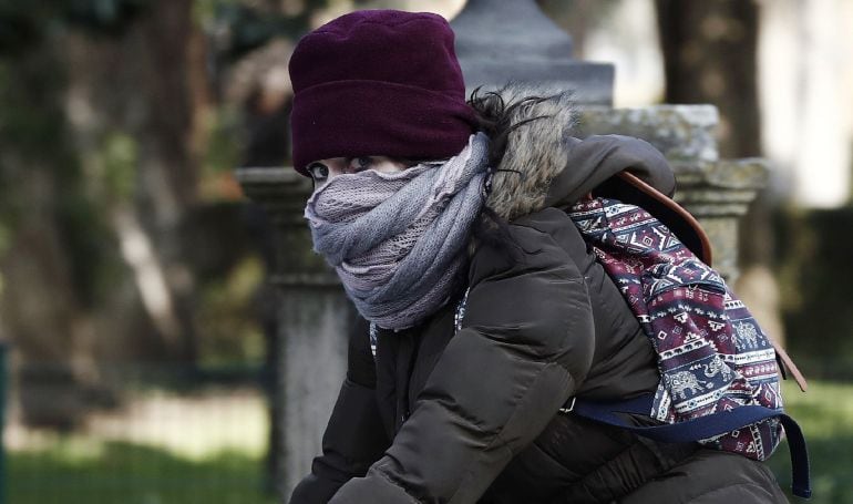 Una joven montada en su bicicleta se protege del frío en Pamplona.