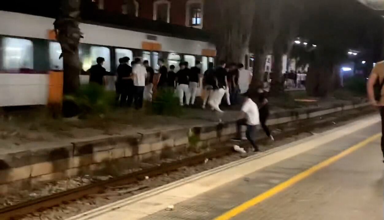 Imatge d'un grup de joves travessant les vies a Mataró i esperant que acabi de passar un tren en sentit Barcelona.