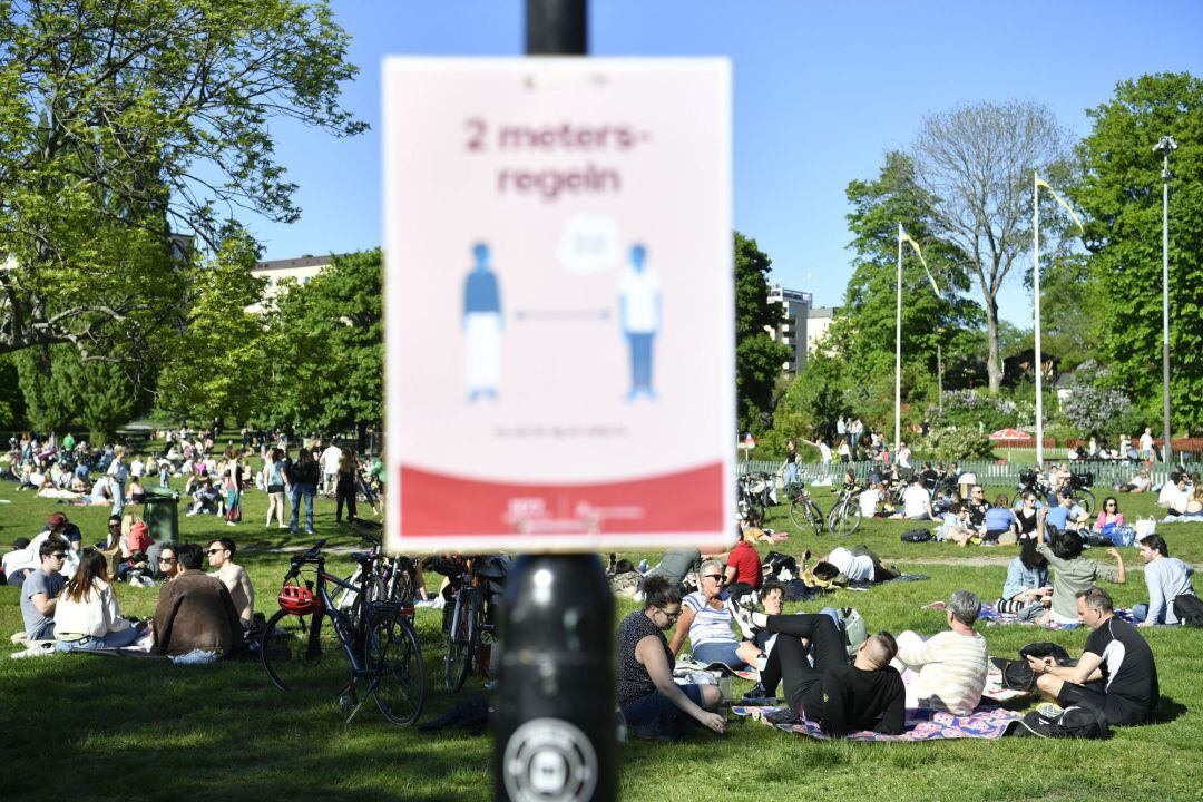 Aglomeración de gente en el parque Tantolunden de Estocolmo (Suecia) y un cartel que avisa de la distancia de seguridad 