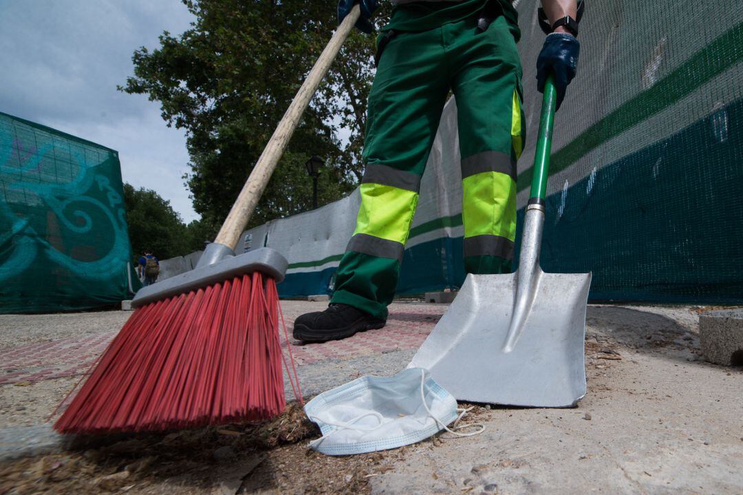 Un trabajador de la limpieza recoge una mascarilla tendida en el suelo de Madrid.