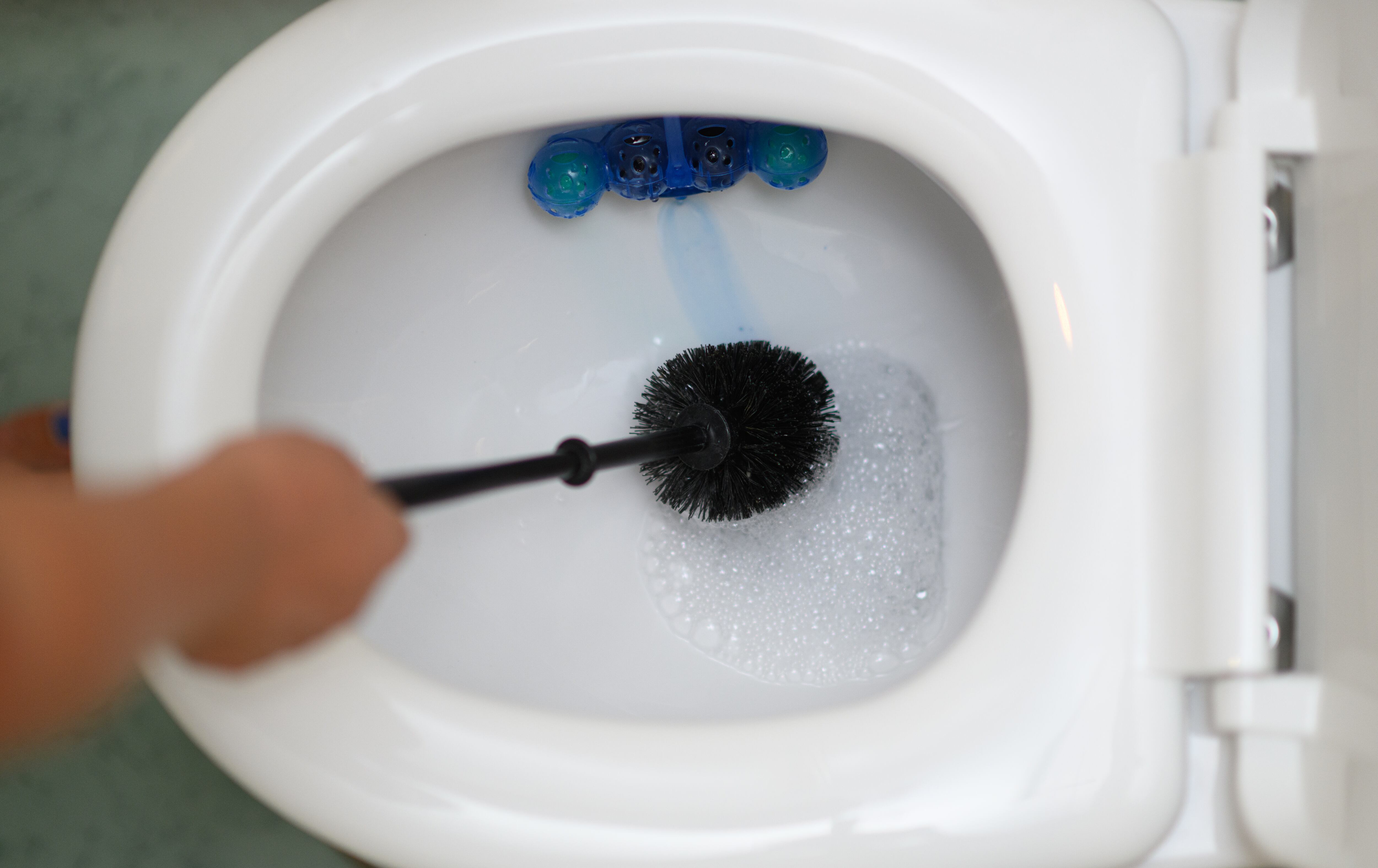 Una persona limpiando el váter con una escobilla.