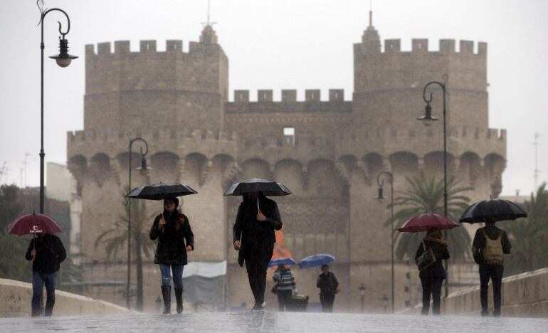 Varias personas cruzan el puente de Serranos bajo la lluvia que durante la mañana de hoy ha caido intermitentemente en gran parte de la Comunidad Valenciana.