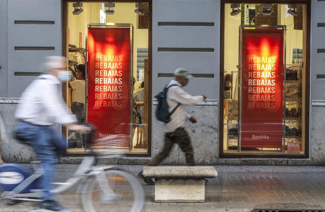 Varias personas pasan al lado del escaparate de una tienda donde se observan carteles indicativos de rebajas en Valencia, Comunidad Valenciana