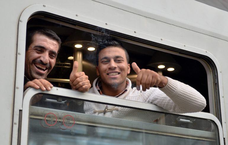 Dos refugiados saludan desde un tren con destino a Freilassing, Alemania, en la estación de Salzburgo