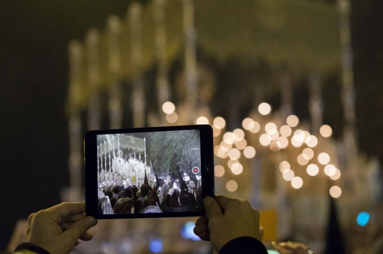  Una persona graba con su tableta el paso de palio de la Esperanza de Triana tras cruzar el puente camino de la carrera oficial, en su recorrido procesional por la calles de Sevilla en la tradicional "Madrugá". 