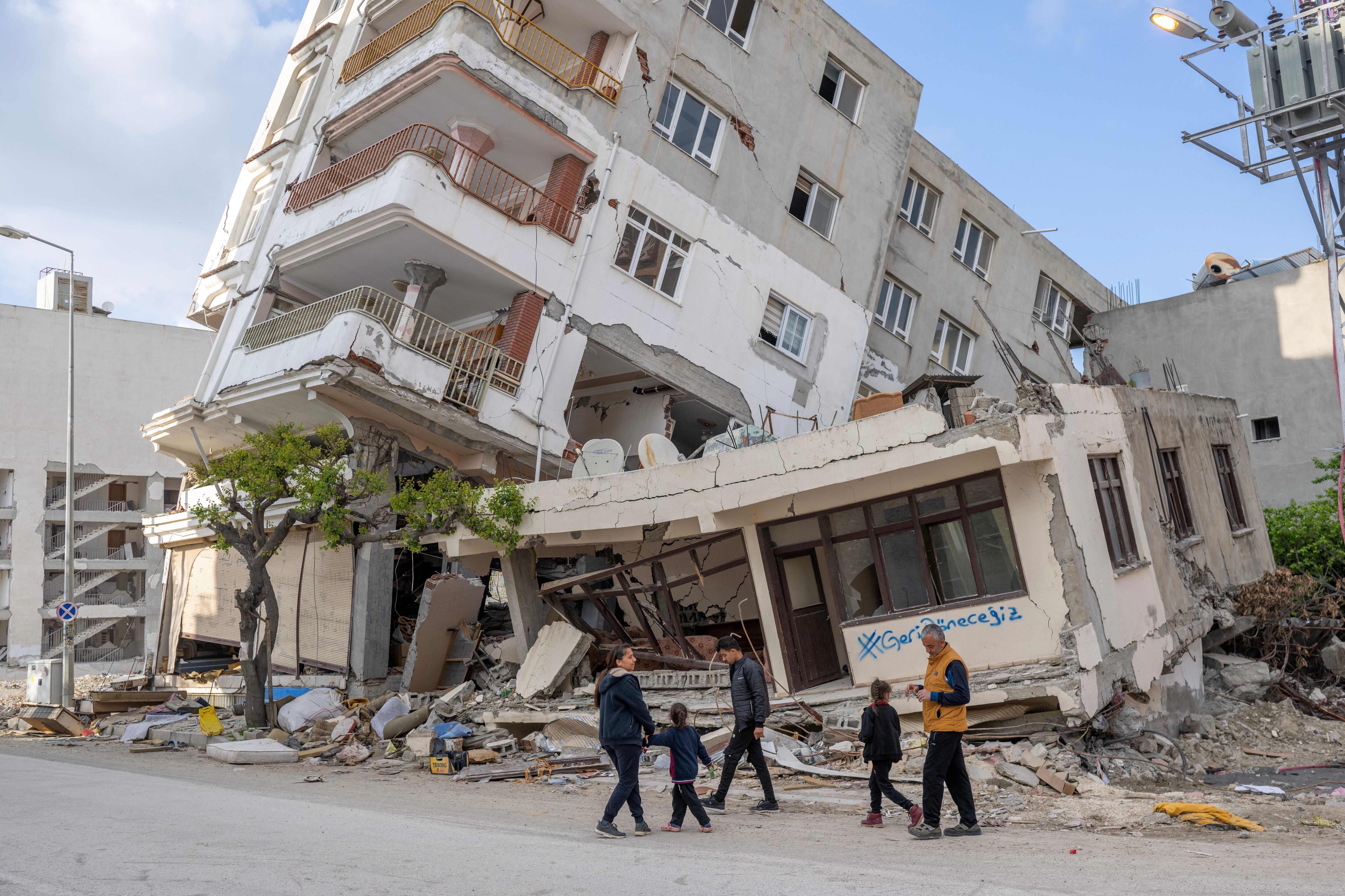 TOPSHOT - Kenan Civi and his family gather in front of their damaged house bearing a graffiti inscription which reads &quot;we will come back&quot;, in Hatay on March 28, 2023, after a 7.8-magnitude earthquake struck on February 6, 2023 killing more than 50,000 in southeastern Turkey and nearly 6,000 over the border in Syria, and leaving entire cities in ruins. - Hundreds of thousands of workers in Turkey and Syria have lost their livelihoods due to the earthquake, the United Nations said on March 28, 2023, as it called for urgent support to rebuild businesses. (Photo by BULENT KILIC / AFP) (Photo by BULENT KILIC/AFP via Getty Images)