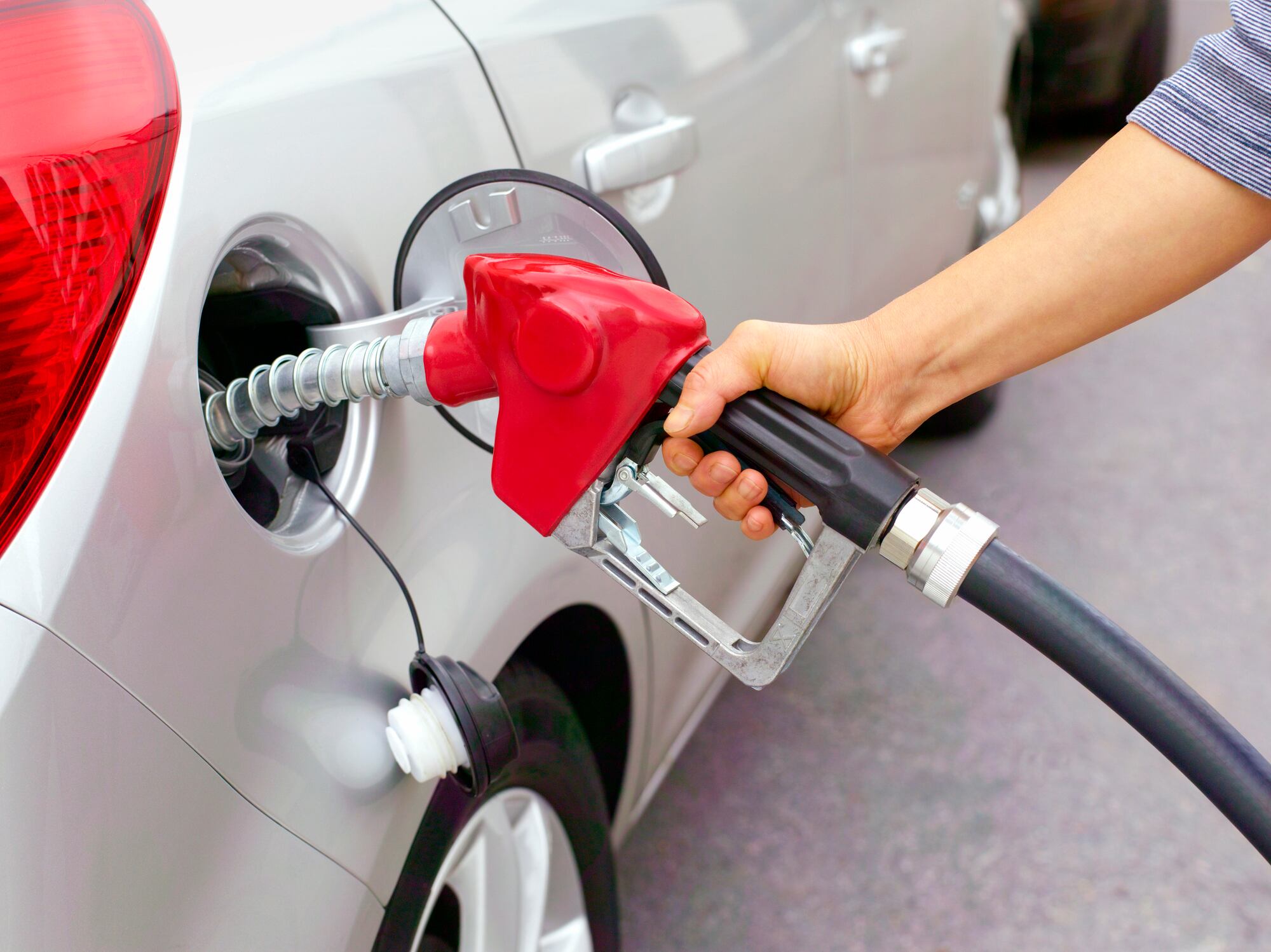 Una mujer echando gasolina a un vehículo en una gasolinera