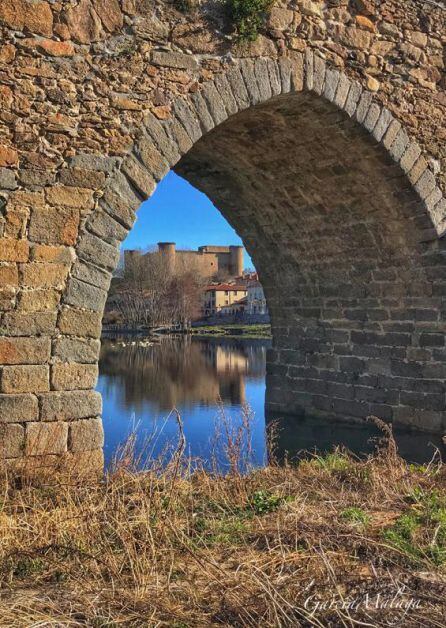 El Castillo de Valdecorneja visto desde uno de los ojos del puente medieval que cruza El Tormes