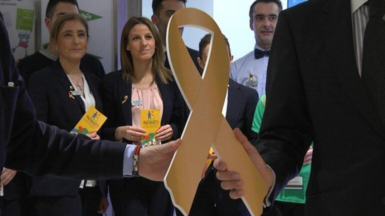 El presidente de la Asociación de Ayuda a Niños Oncológicos de Galicia y el director de marketing de El Corte Inglés sostienen el símbolo contra el cáncer infantil