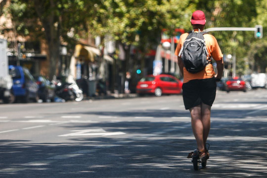 Un hombre cicula en un patinete por una calle por la calzada