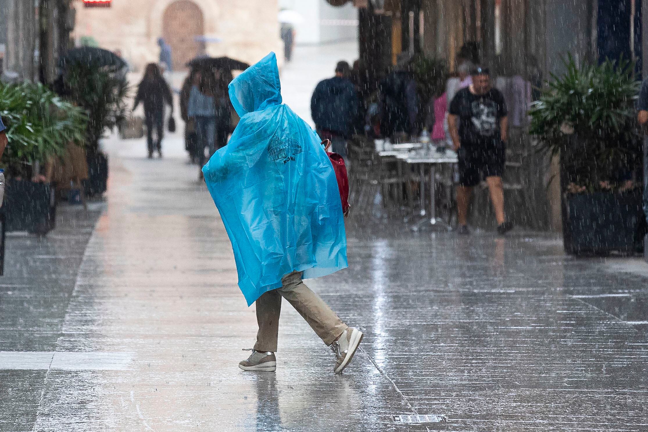 Una mujer se protege de la lluvia con un chubasquero, este martes en la calle Trapería de Murcia.