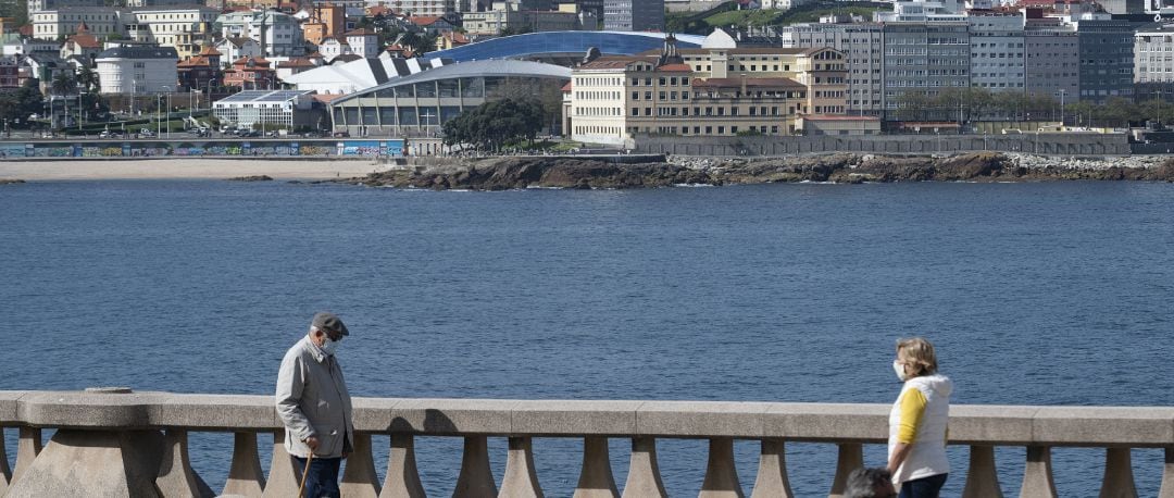 Dos personas pasean por el paseo marítimo de A Coruña en un día de sol