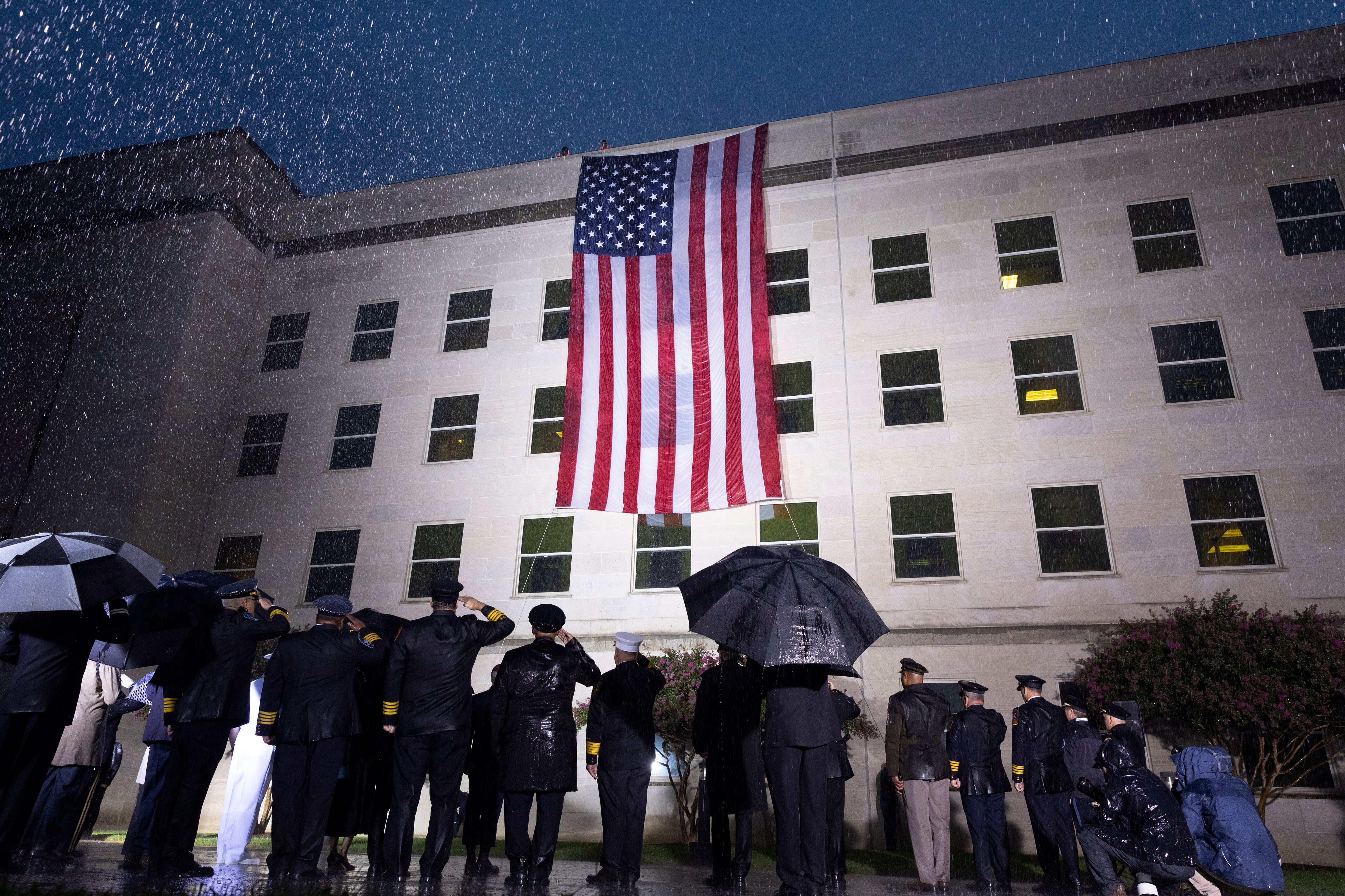 Supervivientes y miembros del Ejército escuchan el himno nacional junto a una bandera desplegada en el Pentágono, en Arlington, Virginia, Estados Unidos este domingo durante el 21º aniversario del atentado a las Torres Gemelas y el Pentágono del 11-S