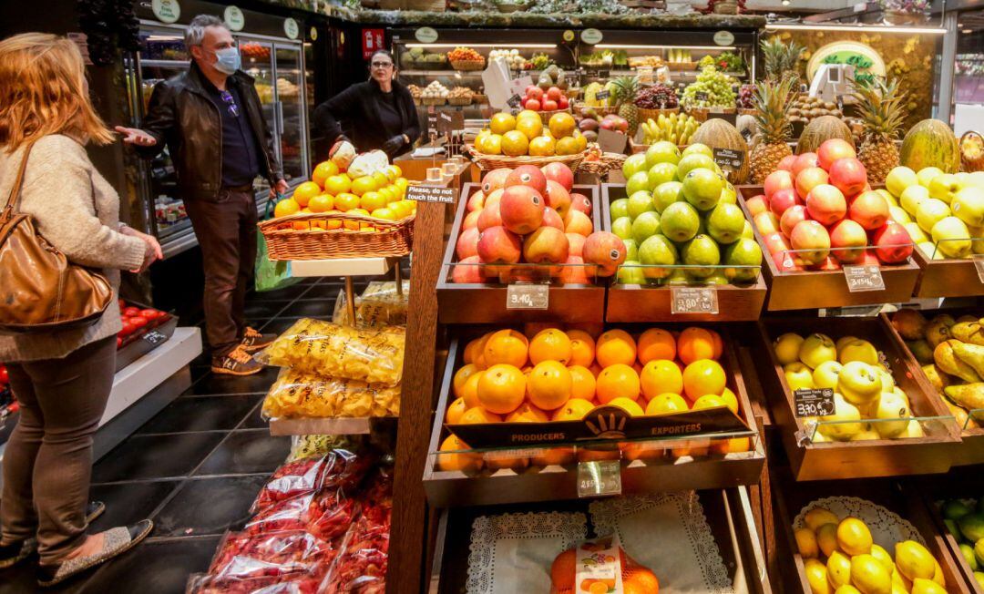 Varios clientes con mascarilla hacen la compra en un puesto de frutas.