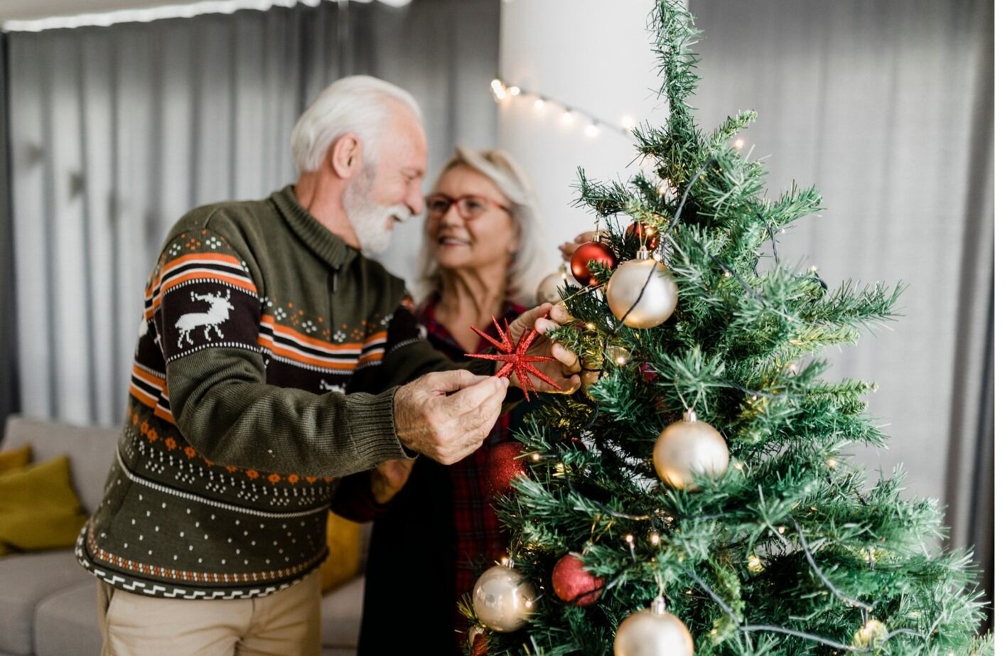 Pareja de personas mayores junto a un árbol de Navidad