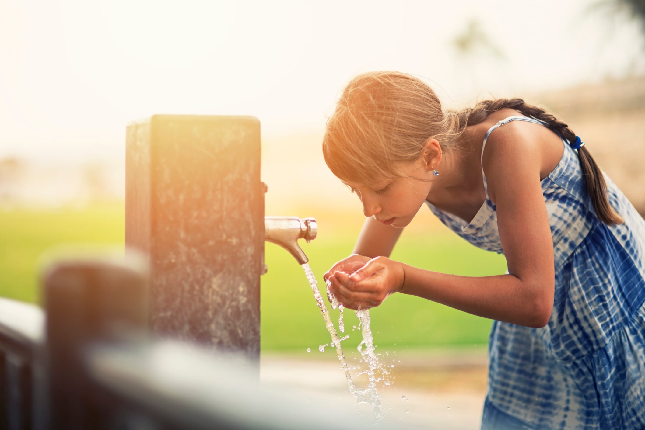 Una niña bebe agua en una fuente