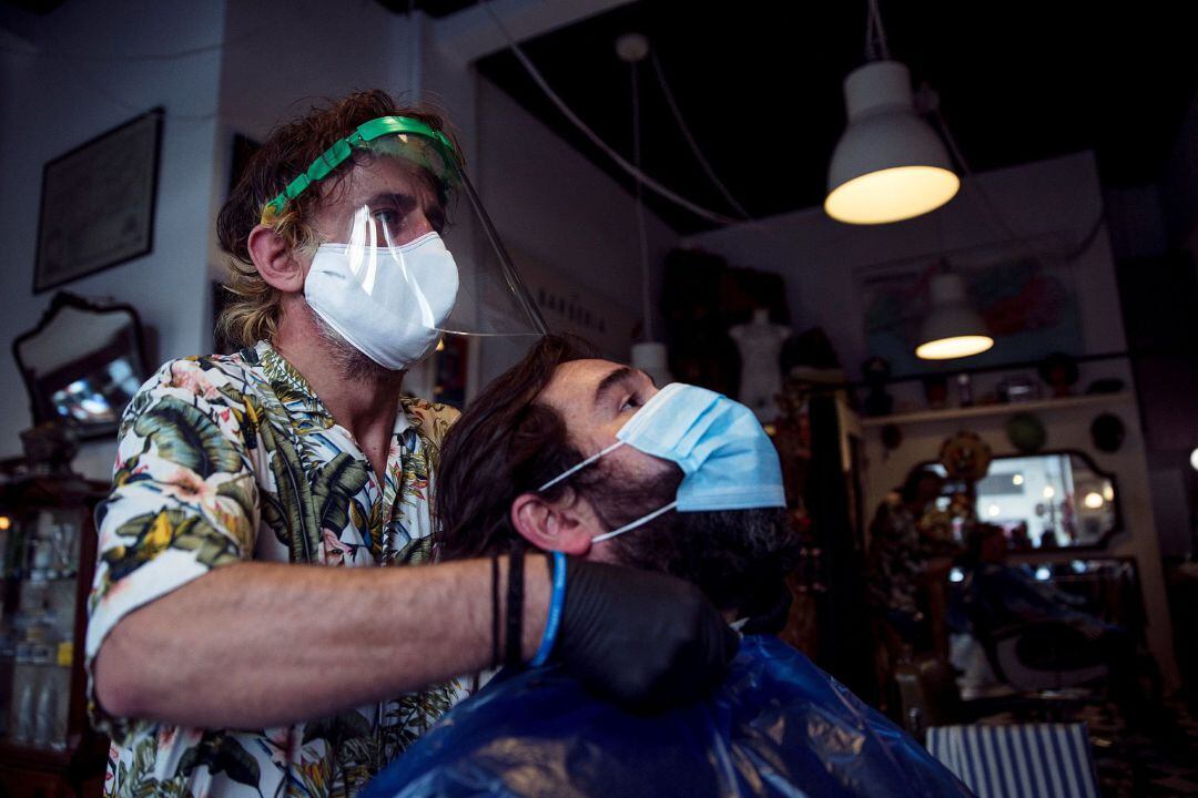 Un peluquero realiza el corte a un cliente en una peluquería del centro de Málaga