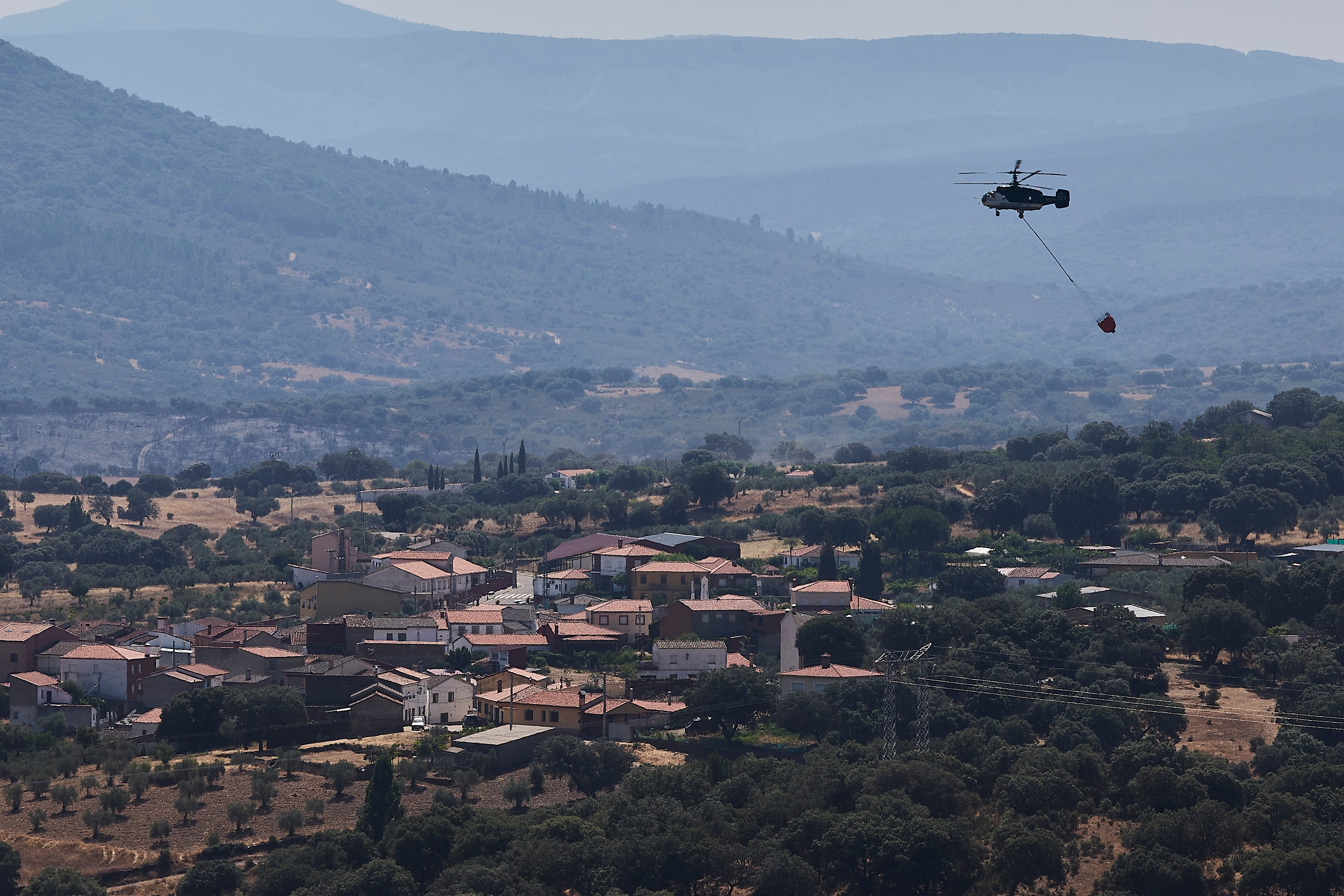 ROBLEDO DEL BUEY(TOLEDO), 30/07/2022.-Vista de un helicóptero trabajando este sábado en la zona del incendio forestal que se originó este viernes en Sevilleja de la Jara (Toledo), que tiene una evolución favorable y, por tanto, a última hora de la tarde se analizará si las 320 personas desalojadas pueden regresar a sus casas.- EFE/Manu Reino
