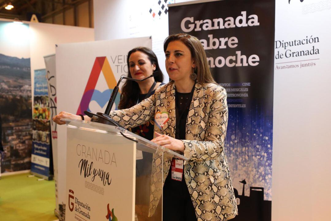 La representante del Centro Comercial Abierto de Granada, María José Mesa Olea, y la concejala de Comercio y Turismo de Granada, Raquel Ruz (en el atril), presentan la Noche en Blanco de Granada en Fitur