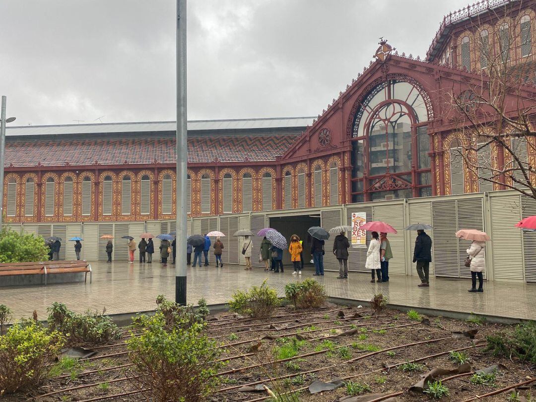 Cola de ciudadanos guardando distancia de seguridad por el coronavirus esperando a votar en el Mercado Sant Antoni de Barcelona 