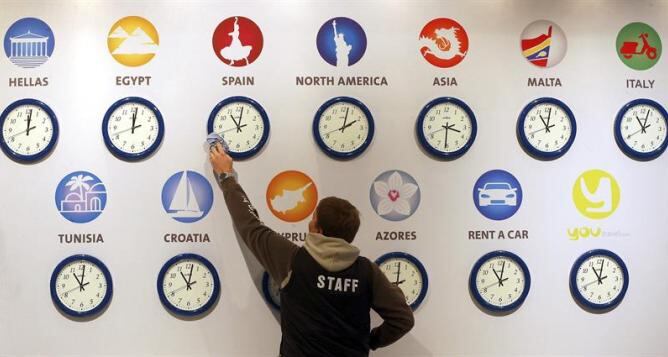 Un trabajador limpia un reloj que refleja la hora en España en la Feria Internacional del Turismo de Berlín (ITB), la mayor del mundo.