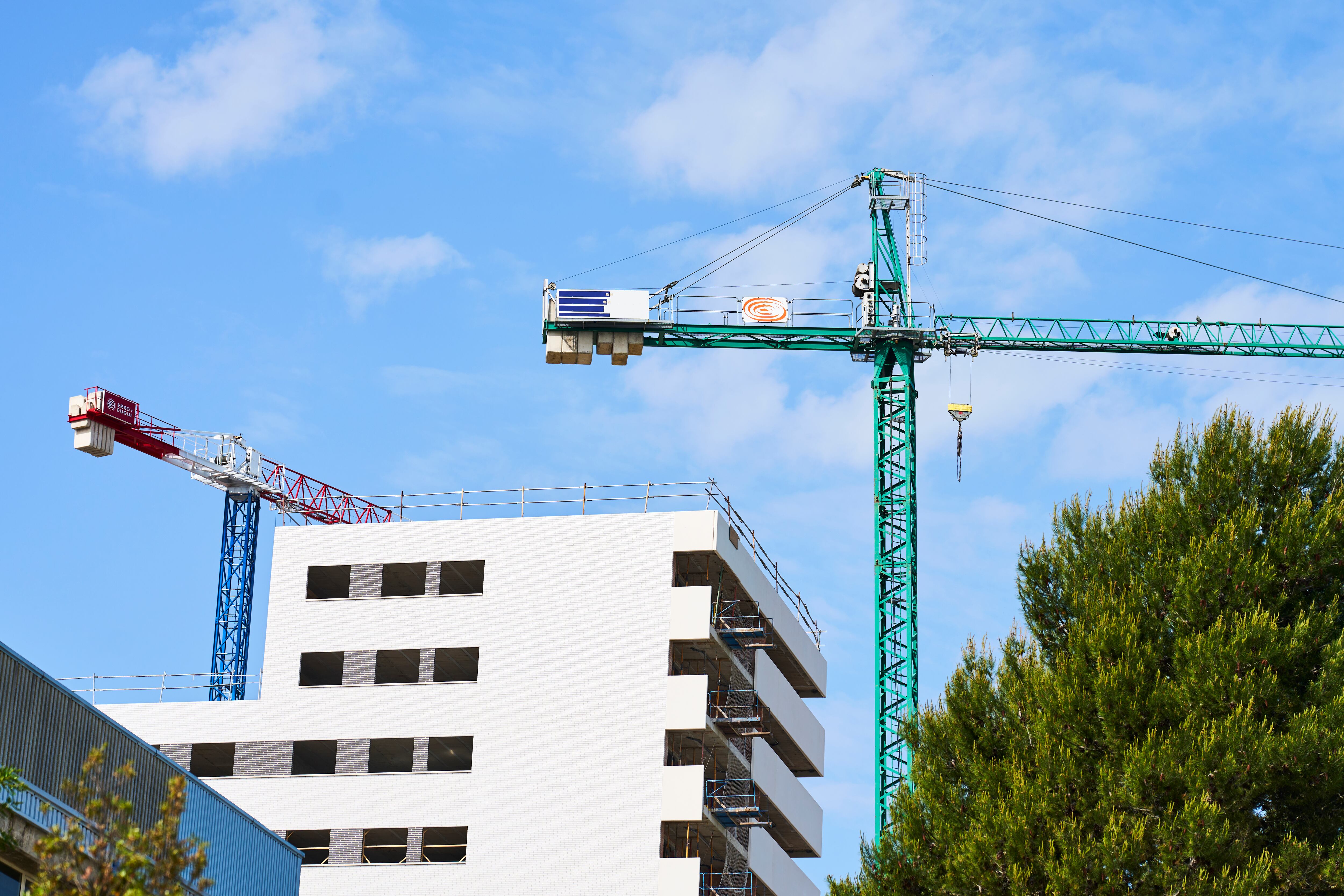 low angle view of a large metal crane in the construction of a building near a park with trees