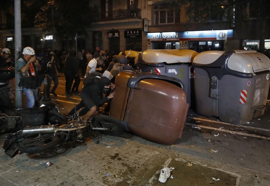 Varios manifestantes vuelcan contenedores durante los disturbios.