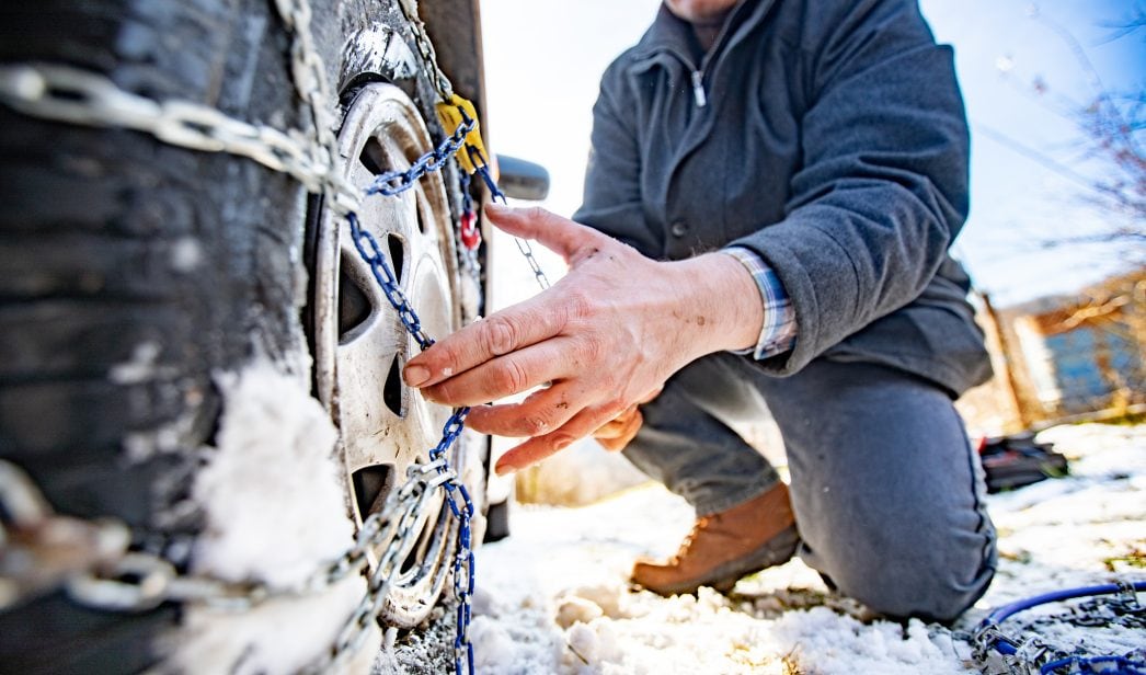 Una persona pone las cadenas de nieve en la rueda del coche.