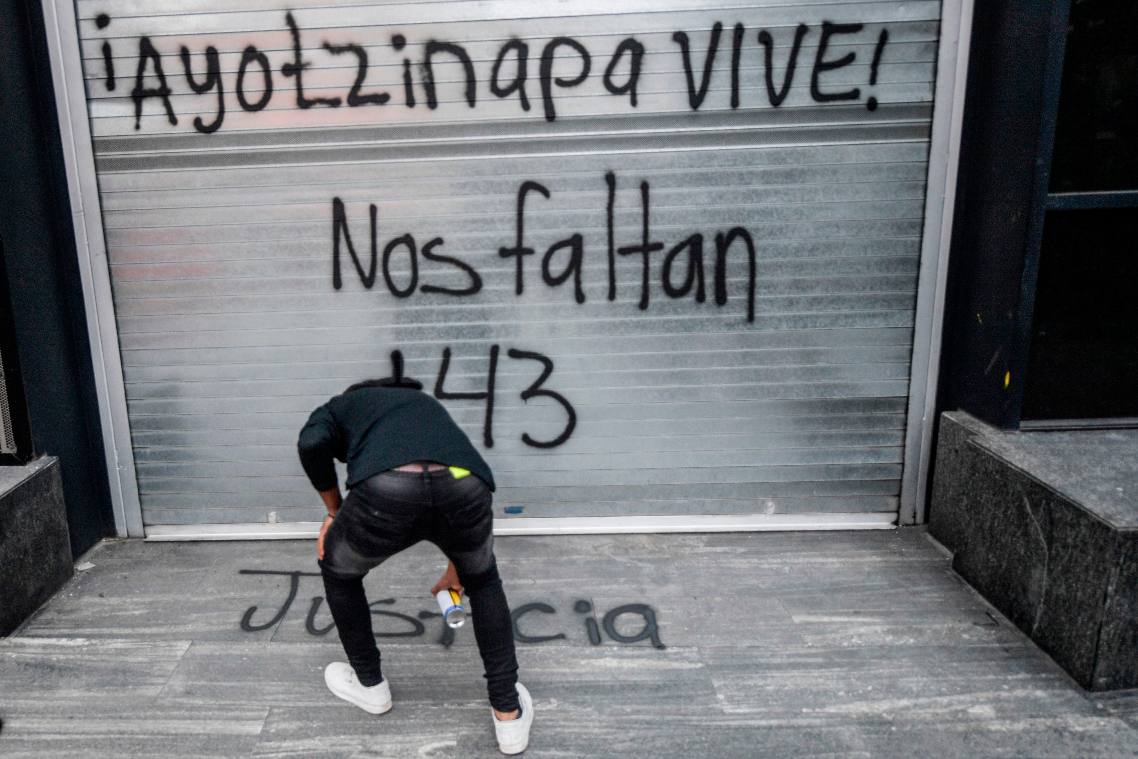 Un manifestante pinta un grafiti en la fachada de la Procuraduría General de la República en Ciudad de México el 25 de septiembre de 2020, durante una protesta en la víspera del sexto aniversario de la desaparición de los 43 estudiantes de la Escuela Normal de Ayotzinapa.