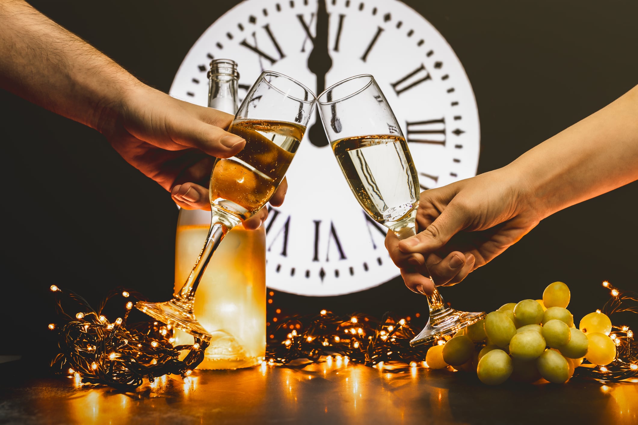 Couple toast to the new year with two glasses of champagne. Celebrating New Year&#039;s Eve. Lucky grapes. Spanish tradition in which 12 grapes are eaten with the last 12 chimes of the year.