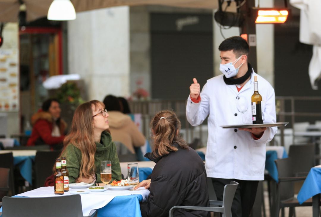 Un camarero atiende a dos clientas en la terraza de un bar.