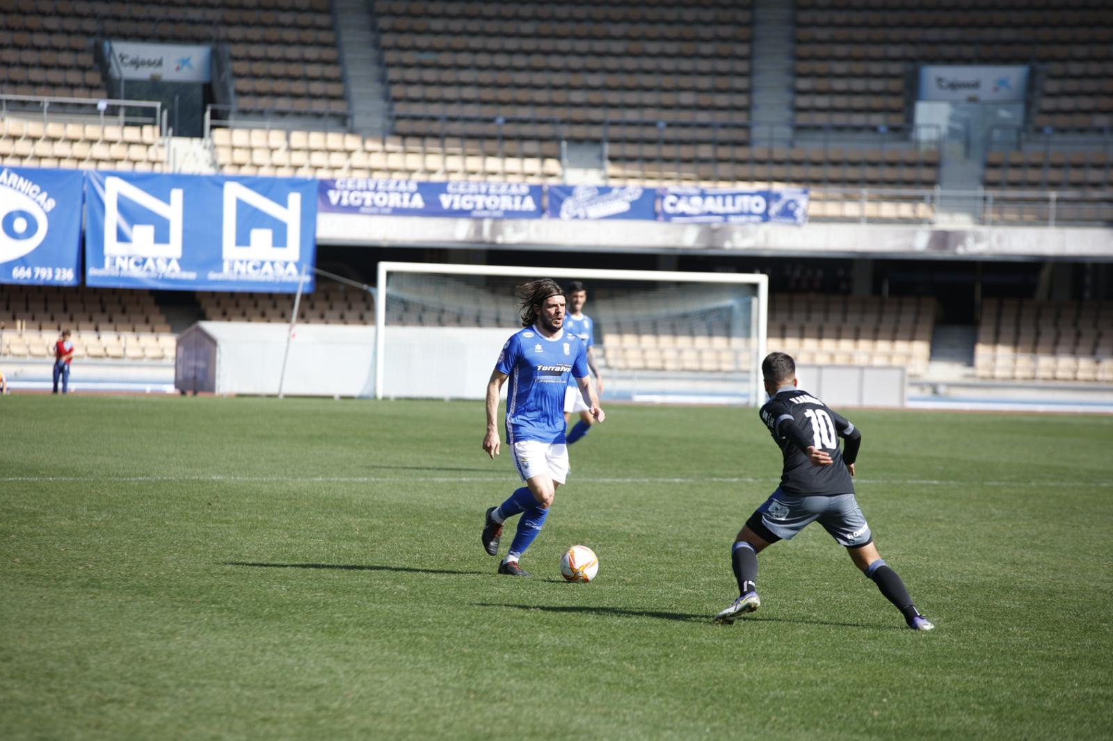 Migue García conduciendo un balón ante un jugador del Recre