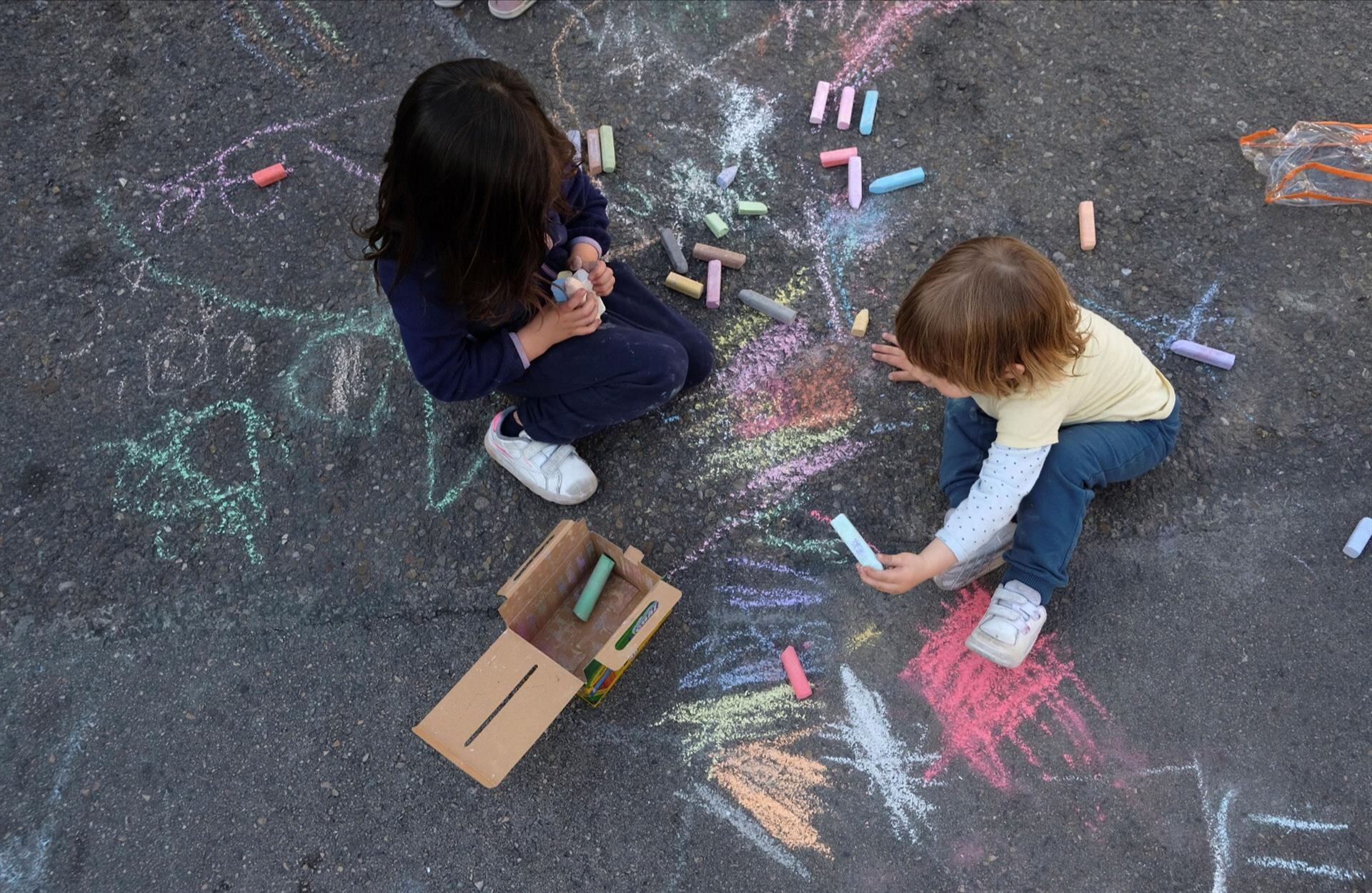 Dos niños juegan sobre el asfalto de la calle junto a un colegio en Madrid.
