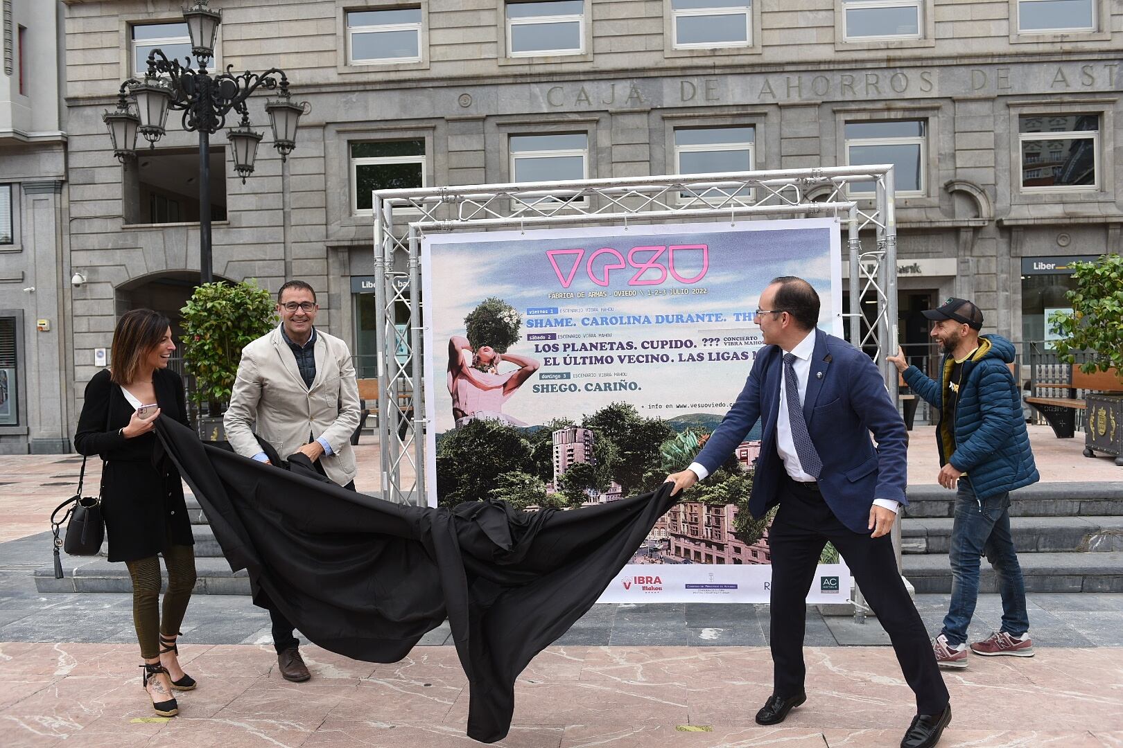 Los concejales Lourdes García, José Luis Costillas y Mario Arias, junto a Íñigo Domínguez, descubren la lona con el cartel del VESU instalada en la plaza de La Escandalera