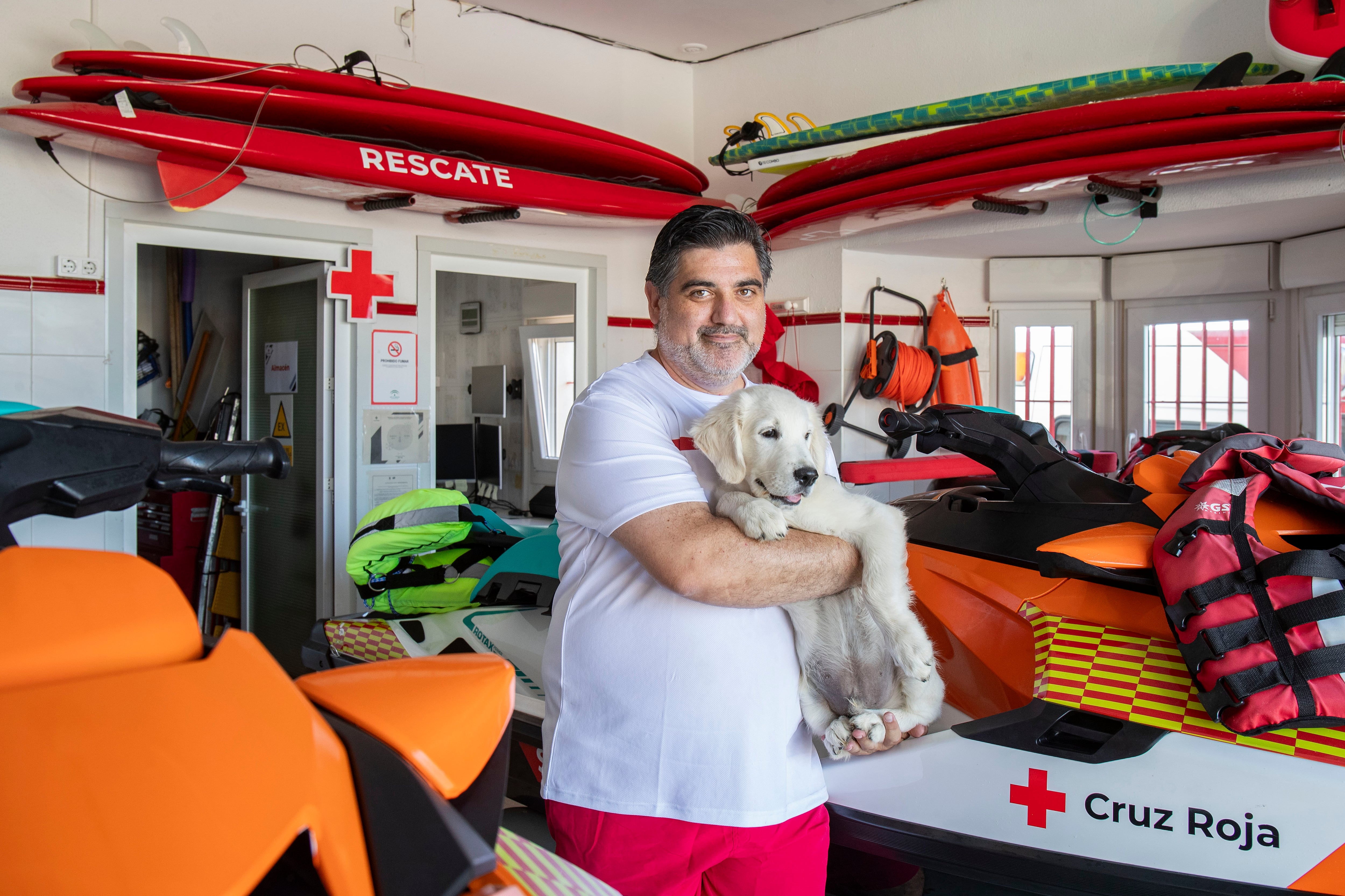 CHICLANA DE LA FRONTERA (CÁDIZ), 04/08/2023.- El cuidador y preparador canino, Juan Luis de Castellví, junto a Chui, un cachorro de Golden Retriever que se prepara como apoyo a los socorristas del puesto de la Cruz Roja en la playa de La Barrosa en Chiclana de la Frontera, este viernes, y que se convertirá en el primer socorrista canino de la Cruz Roja en España. EFE/ Román Ríos
