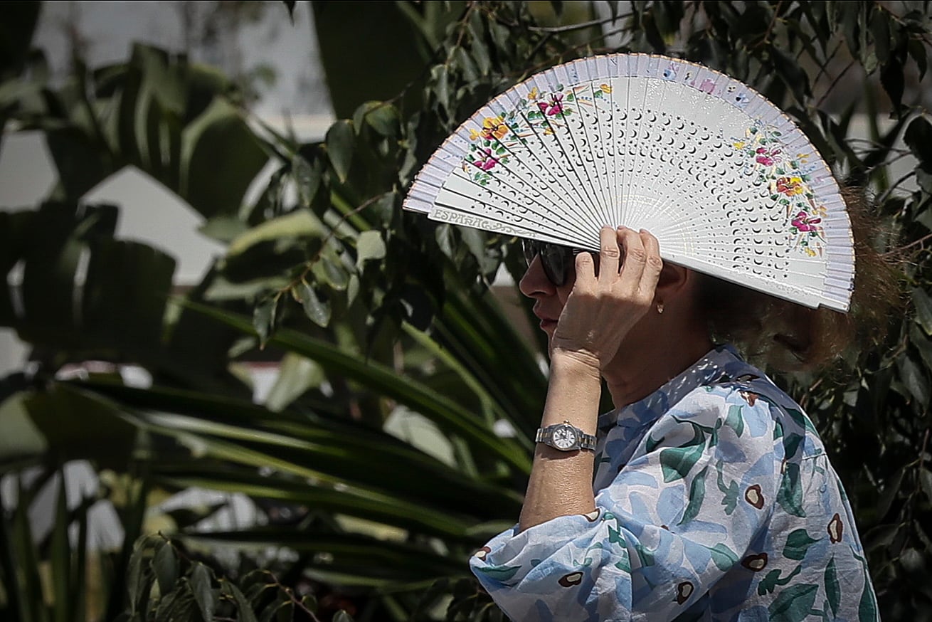 Una persona se cubre la cabeza con un abanico para paliar los rayos del sol directos mientras camina por Sevilla