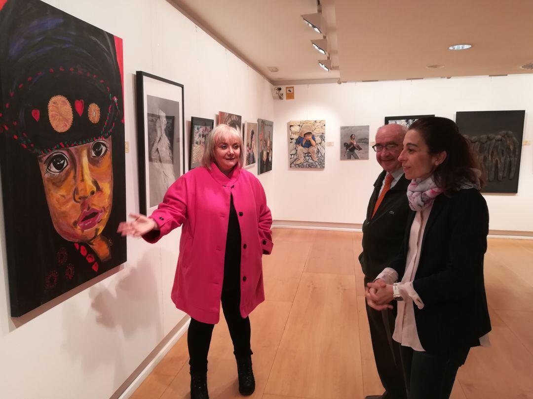Sole Espeja muestra el cuadro que aporta a esta exposición a Laura Cabañes, de Caja de Burgos y Pedro Benito, de Cruz Roja