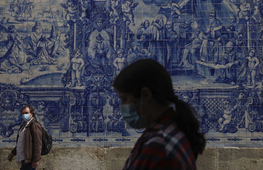 Dos personas caminan por una calle de la ciudad de Oporto con mascarilla.