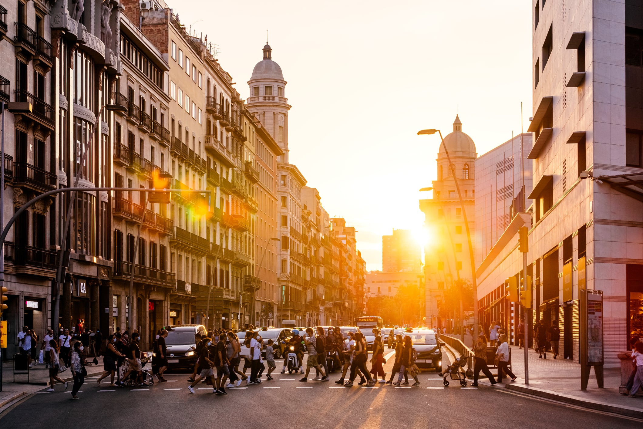 Decenas de personas cruzan una calle, durante un día soleado, en Barcelona.